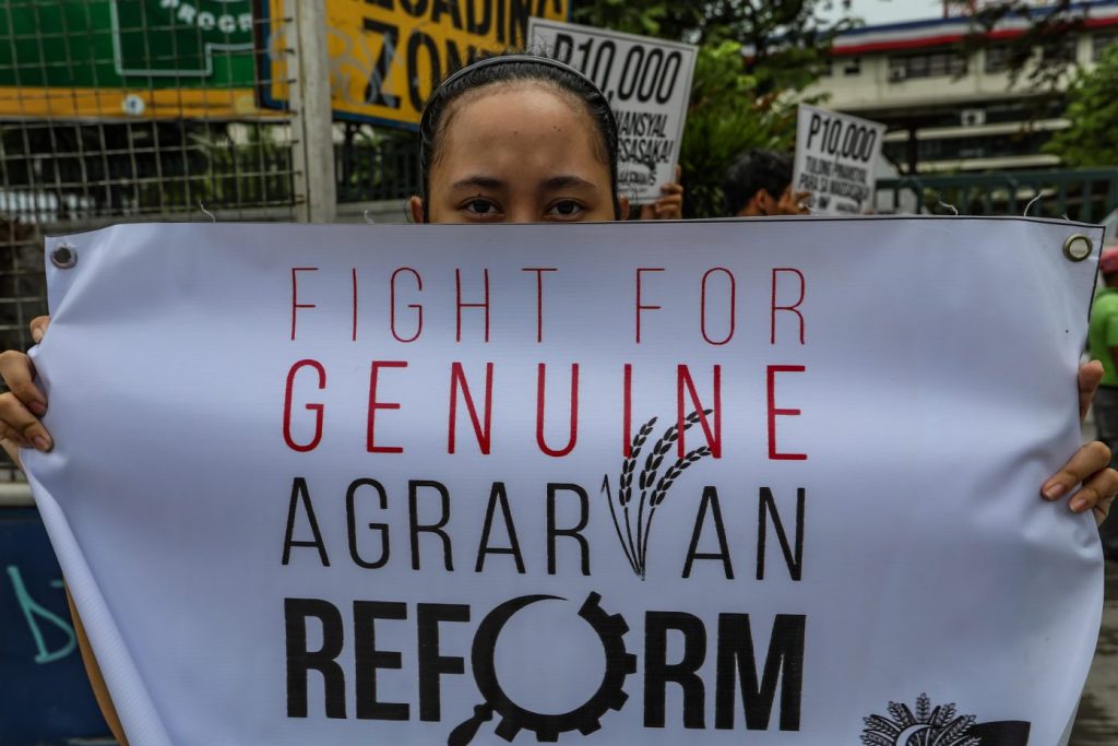A protester holding a placard saying "Fight for Genuine Agrarian Reform"